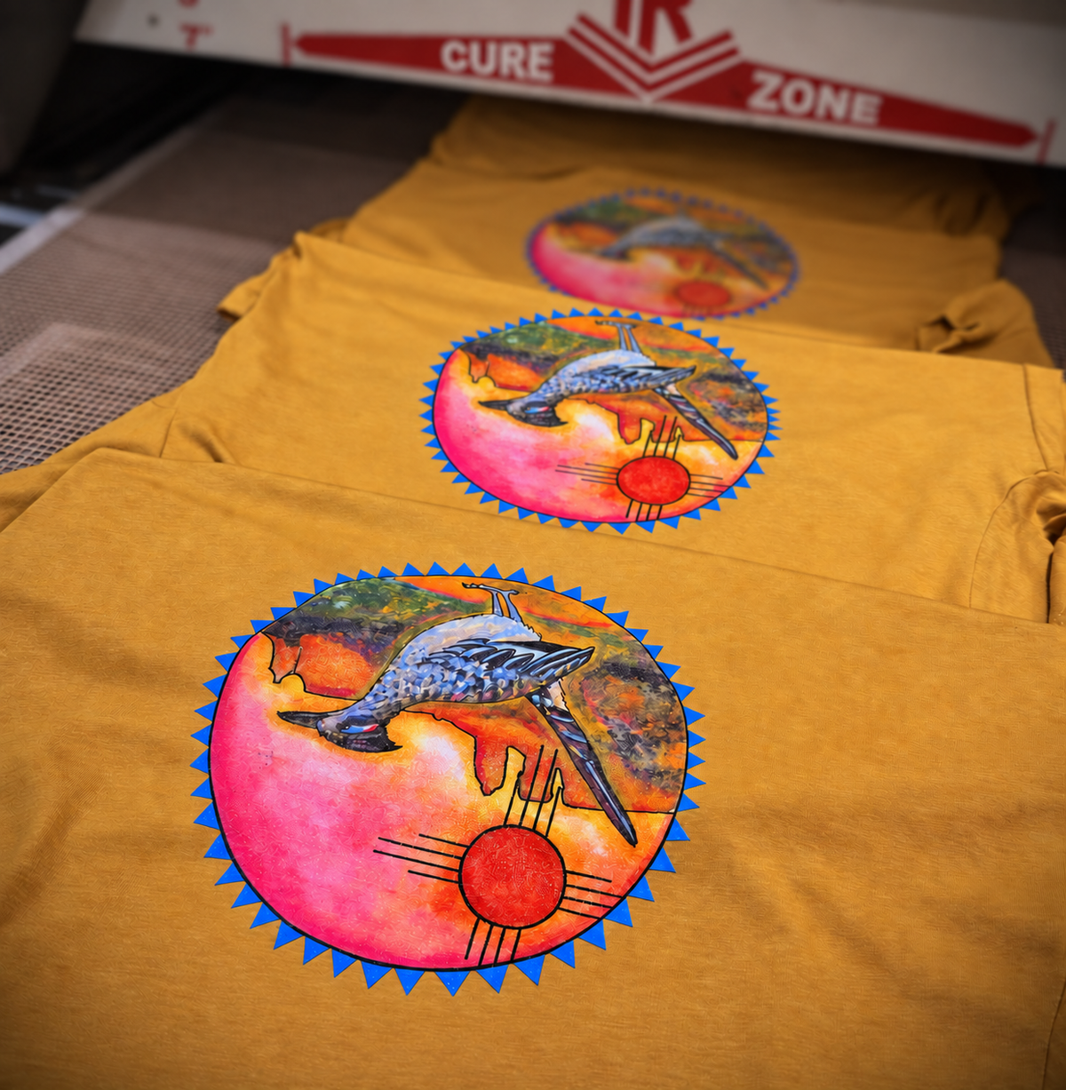 Three golden shirts with colorful roadrunner prints passing through a conveyor dryer